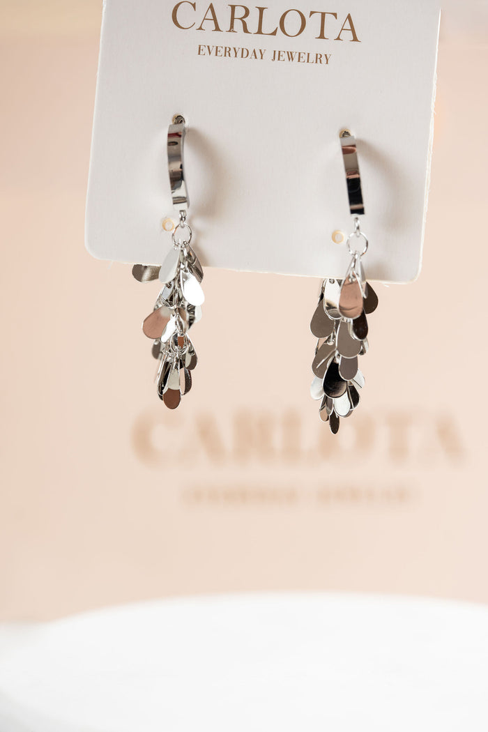 Aros plateados con varios dijes que caen y bolsa de CARLOTA Joyería detras