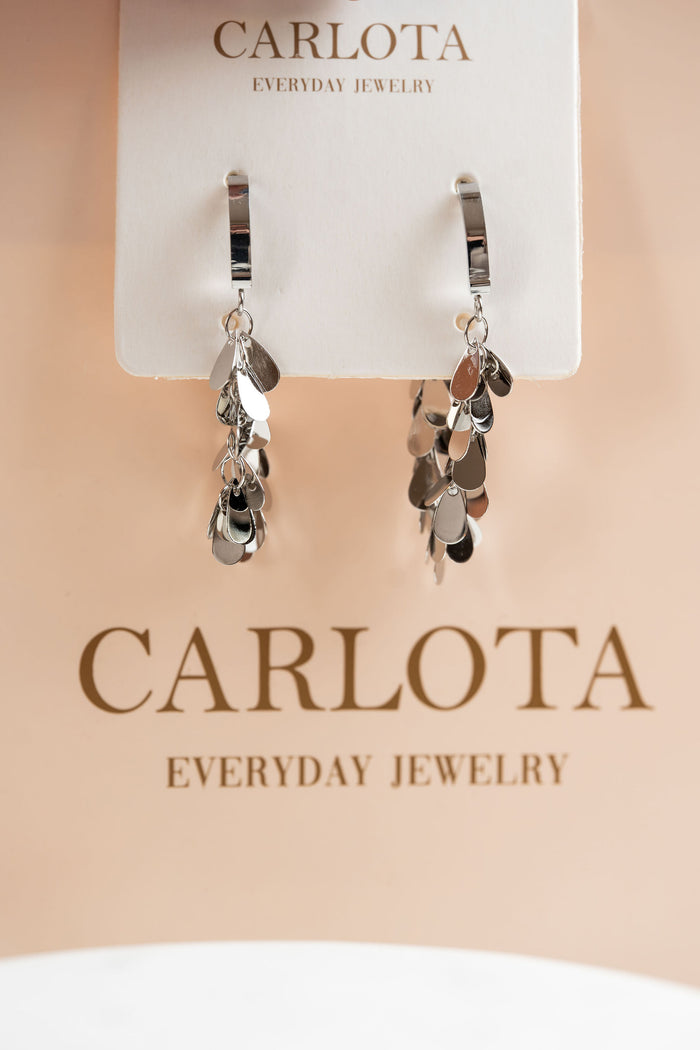 Aros plateados con dijes con bolsa de Joyeria CARLOTA detras
