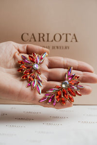 Aros en tonos rojos abiertos con forma geométrica irregular y acabado brillante, en mano | Larisa de CARLOTA.