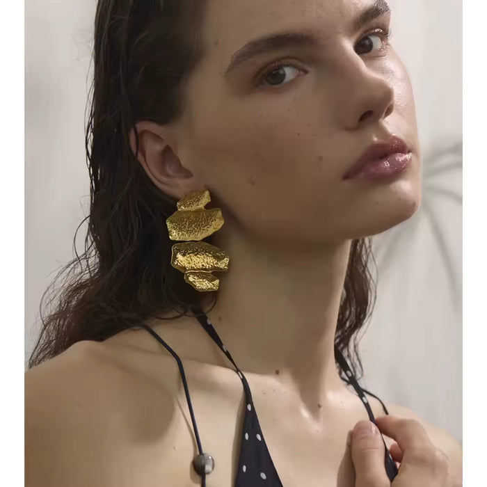 Aros dorados  con colgantes metálicos brillantes en forma de hoja o gota, modelo Mabel de CARLOTA.