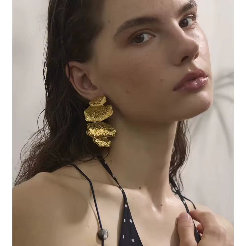 Aros dorados  con colgantes metálicos brillantes en forma de hoja o gota, modelo Mabel de CARLOTA.
