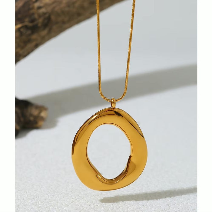 Collar dorado con dije irregular orgánico grande sobre fondo claro
