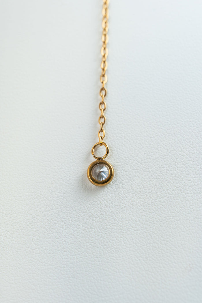 Collar dorado con detalle de piedra brillante en fondo blanco