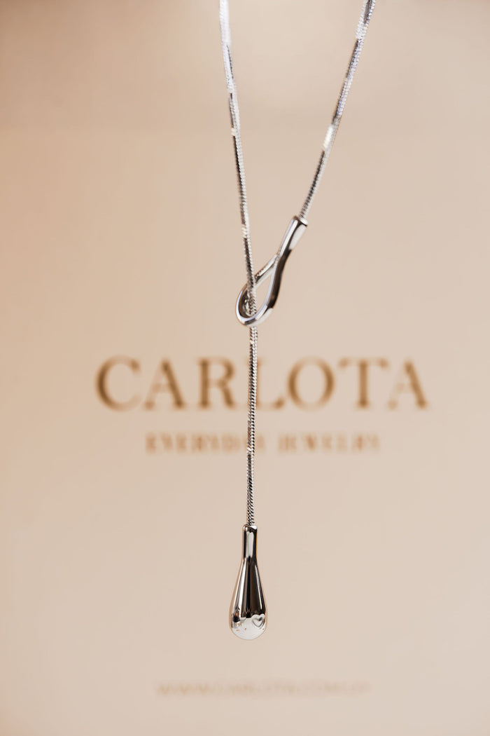 Collar largo de acero quirúrgico en tono plateado con diseño tipo lazo, modelo Débora sin baño de CARLOTA.