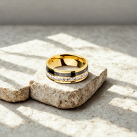 Anillo dorado con doble banda, una con circonias y otra negra con números romanos, sobre base de piedra.