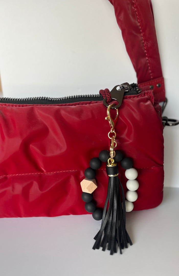 Llavero pulsera negra con cuentas de silicona, dije de madera y flecos de cuero sintético en cartera roja