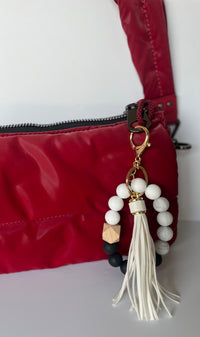 Llavero pulsera elástica con cuentas de silicona blancas y negras y flecos en simil cuero blancos, en cartera roja.