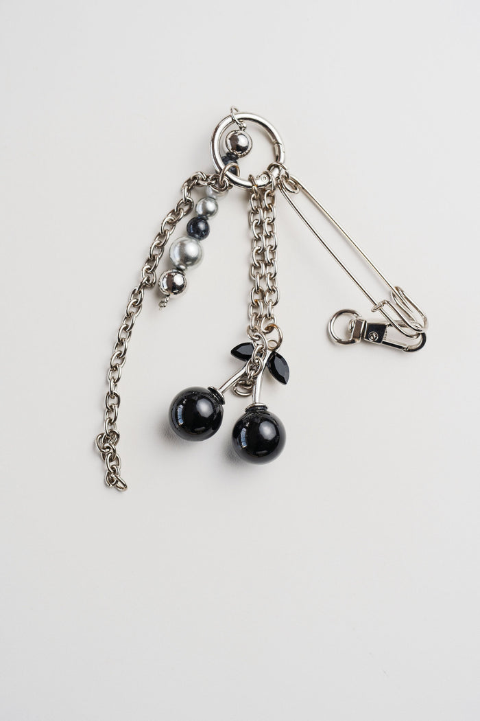 Llavero con cerezas negras brillantes y gancho metálico, sobre fondo rosa claro. Accesorio decorativo con estilo pop y original.
