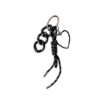 Llavero negro con cinta y dije de corazón, sobre fondo neutro. Ideal como accesorio para llaves, mochila o cartera.