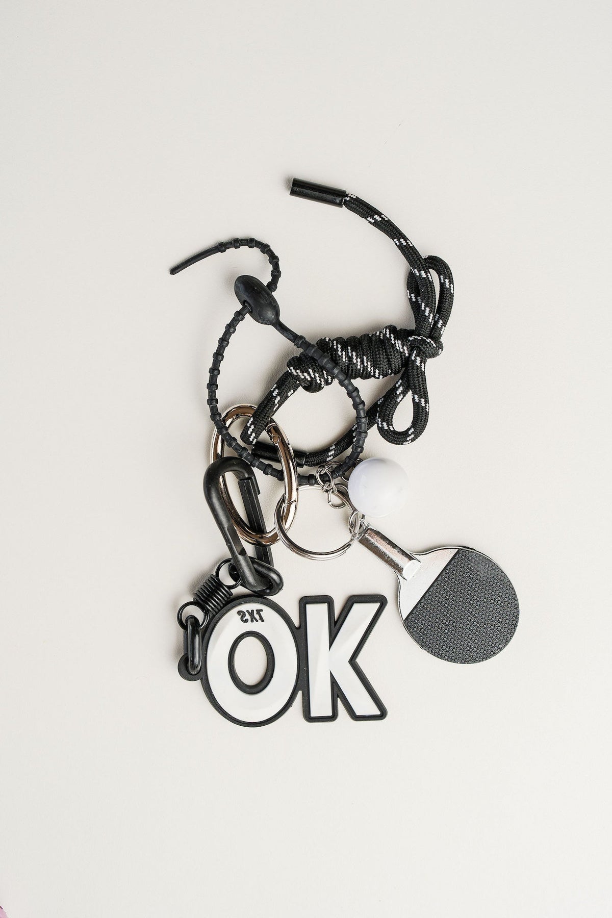 Llavero paddle en metal plateado, cordón negro y simbolo de OK. Ideal para llaves o como accesorio de estilo.