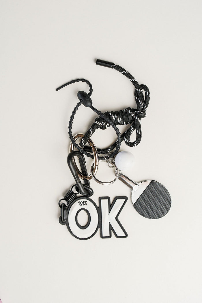 Llavero paddle en metal plateado, cordón negro y simbolo de OK. Ideal para llaves o como accesorio de estilo.