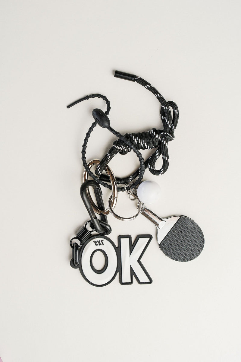 Llavero paddle en metal plateado, cordón negro y simbolo de OK. Ideal para llaves o como accesorio de estilo.