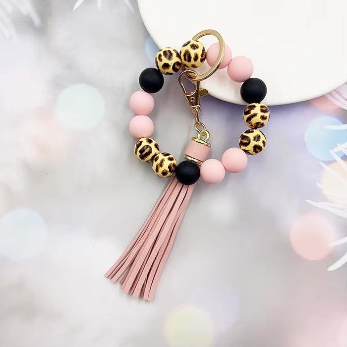 Llavero tipo pulsera con cuentas animal print, cuentas rosa y negras, y colgante de flecos en tono rosa claro.