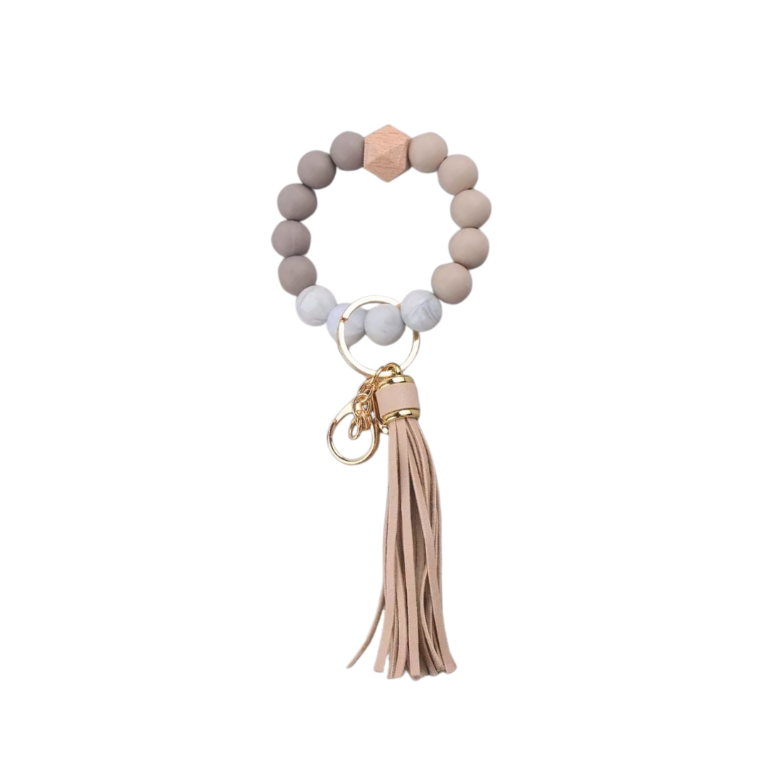 Llavero pulsera nude con cuentas de silicona y flecos, ideal para usar en la muñeca o colgar en cartera.
