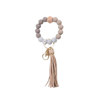 Llavero pulsera nude con cuentas de silicona y flecos, ideal para usar en la muñeca o colgar en cartera.
