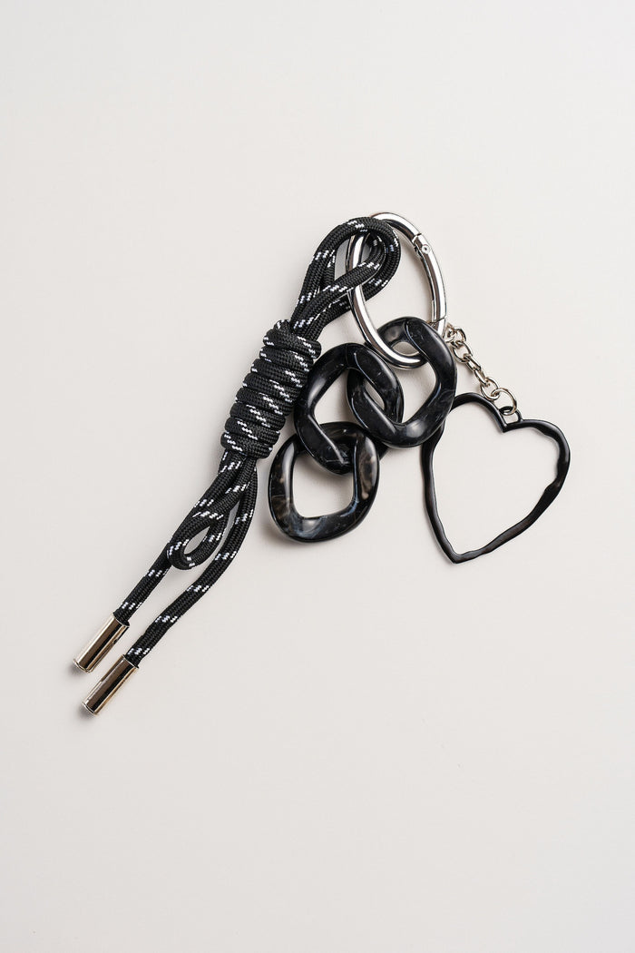 Llavero negro con cordón y dije de corazón, sobre fondo neutro. Ideal como accesorio para llaves, mochila o cartera.