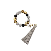 Llavero tipo pulsera con cuentas animal print, cuentas negras y grises, y colgante de flecos en tono gris claro