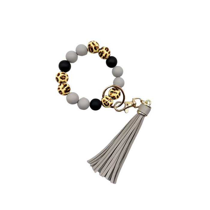 Llavero tipo pulsera con cuentas animal print, cuentas negras y grises, y colgante de flecos en tono gris claro