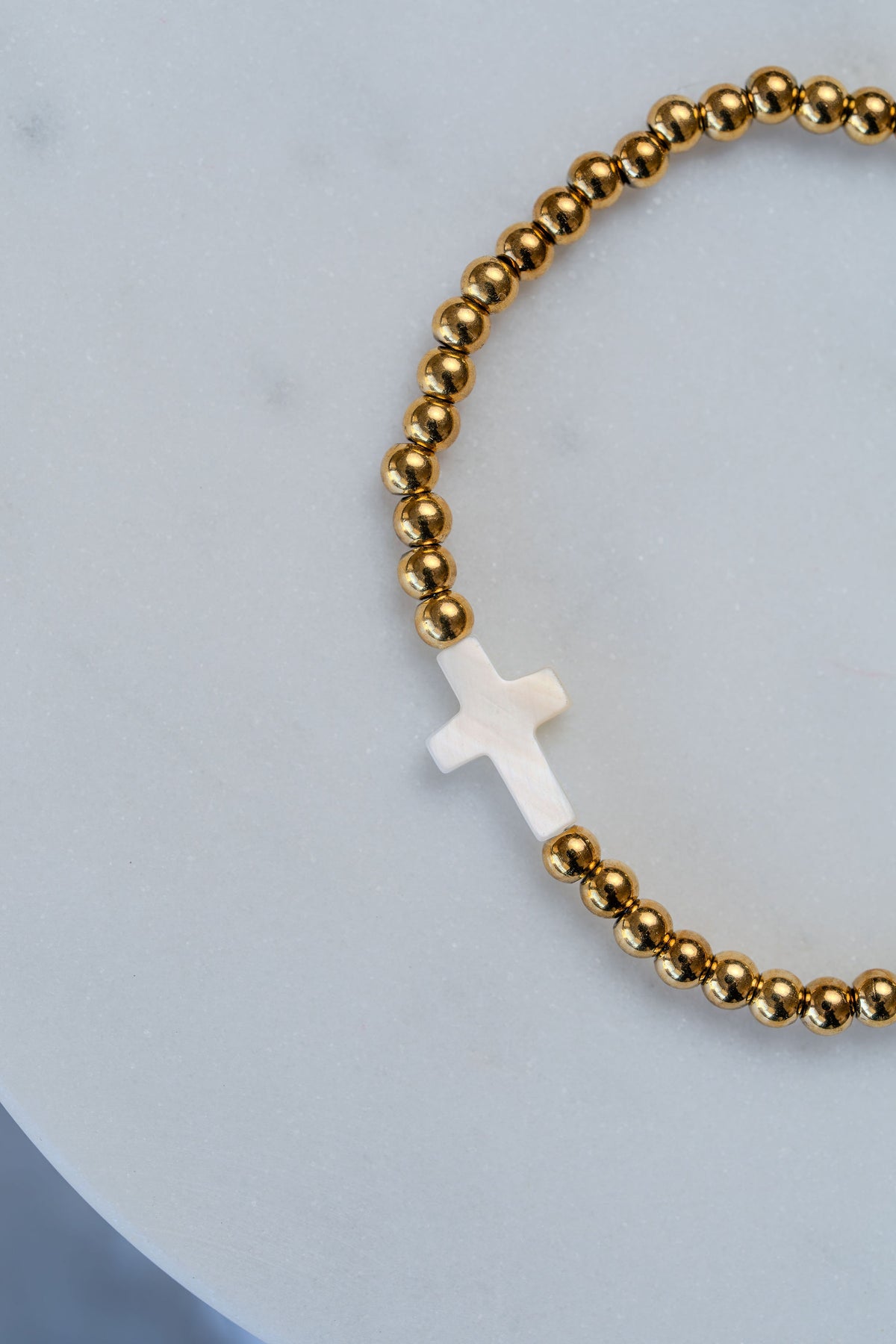 Pulsera de cuentas y cruz de acero dorado en detalle
