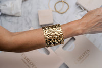 Pulsera ancha abierta de acero dorado y martillada de CARLOTA en modelo
