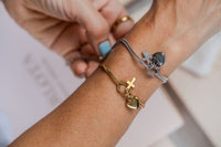 Pulseras de acero con dijes de corazon y cruz en modelo
