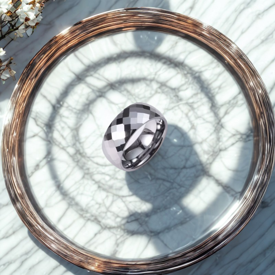 Anillo ancho dorado con acabado facetado brillante sobre bandeja de marmol

