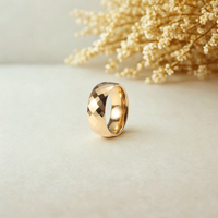 Anillo ancho dorado con acabado facetado brillante sobre fondo neutro