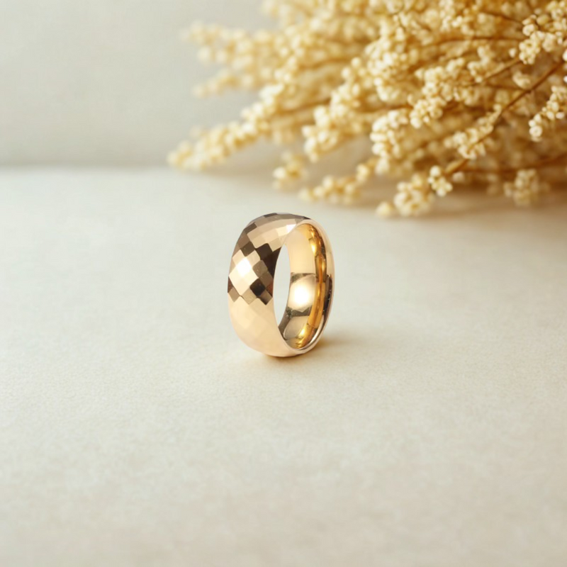 Anillo ancho dorado con acabado facetado brillante sobre fondo neutro