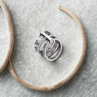 Anillo plateado de triple alianza con detalles de circonias sobre superficie gris