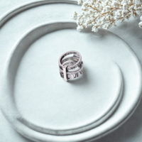 Anillo plateado de triple alianza con detalles de circonias sobre superficie gris