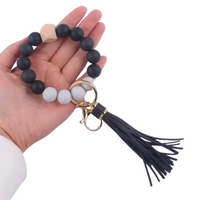 Llavero pulsera negra con cuentas de silicona, dije de madera y flecos de cuero sintético en mano